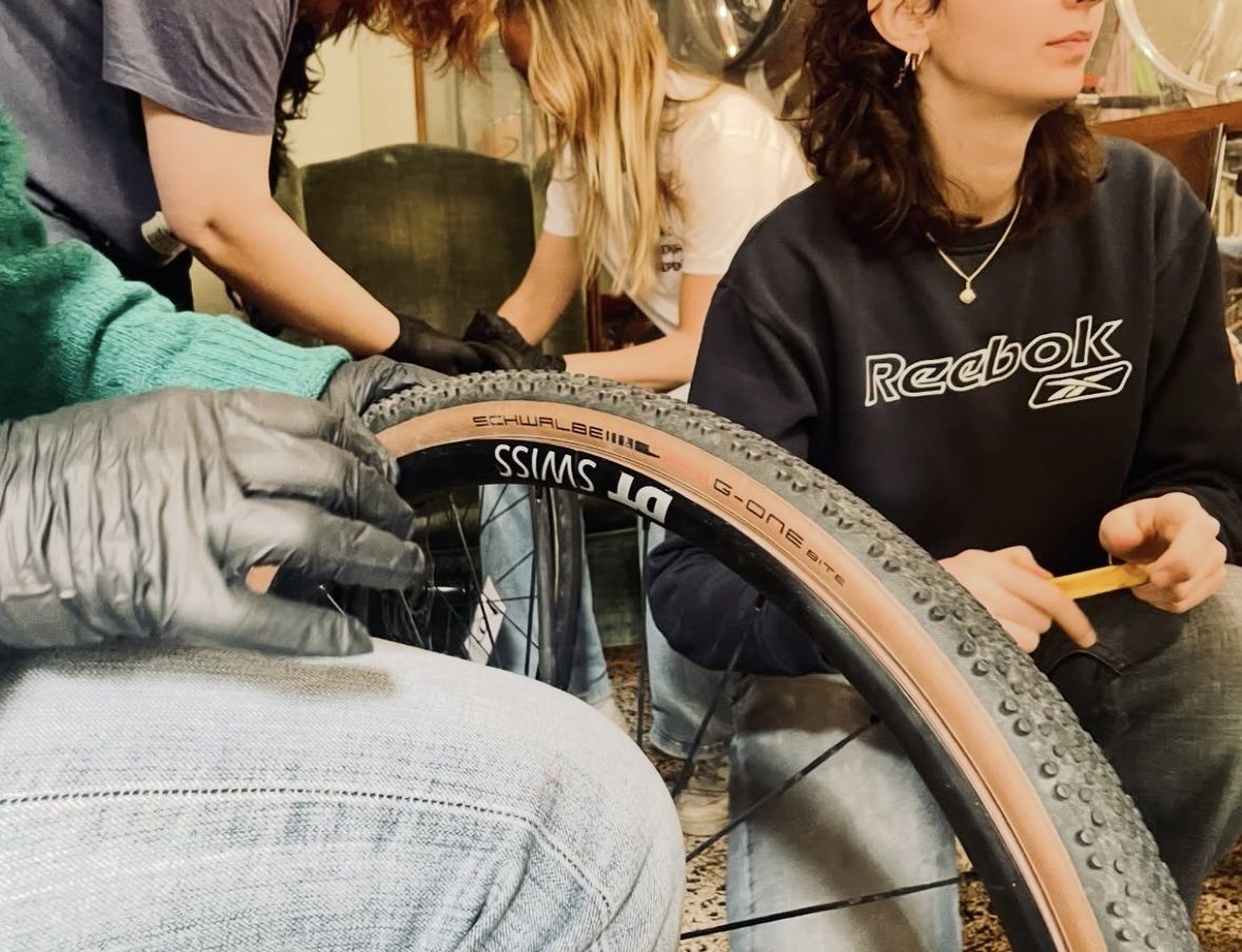 Gloved hands fitting a tyre onto a bicycle wheel rim during a repair workshop in Turin