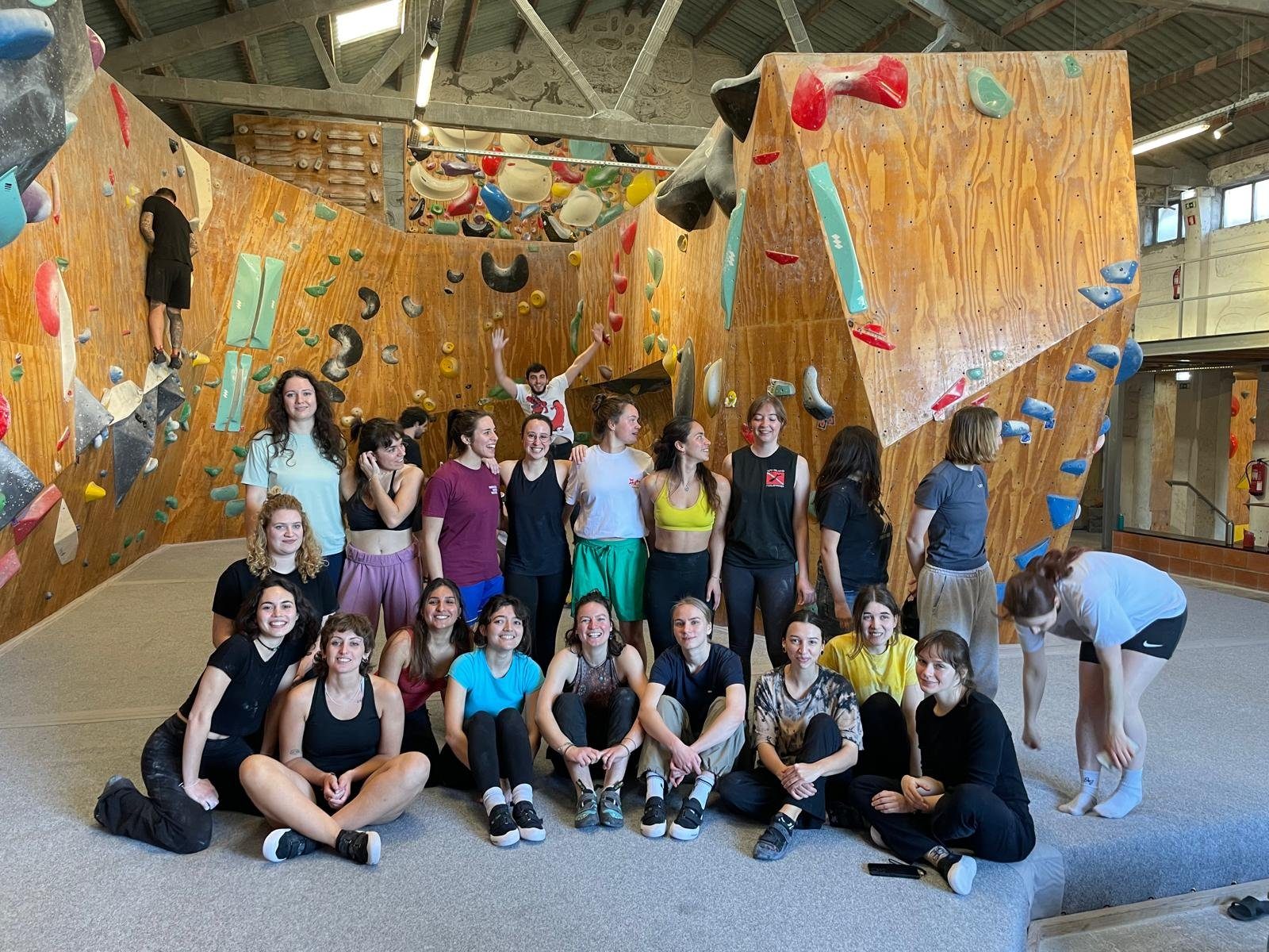 A large group of around twenty women gathered together in front of a bouldering wall in Porto