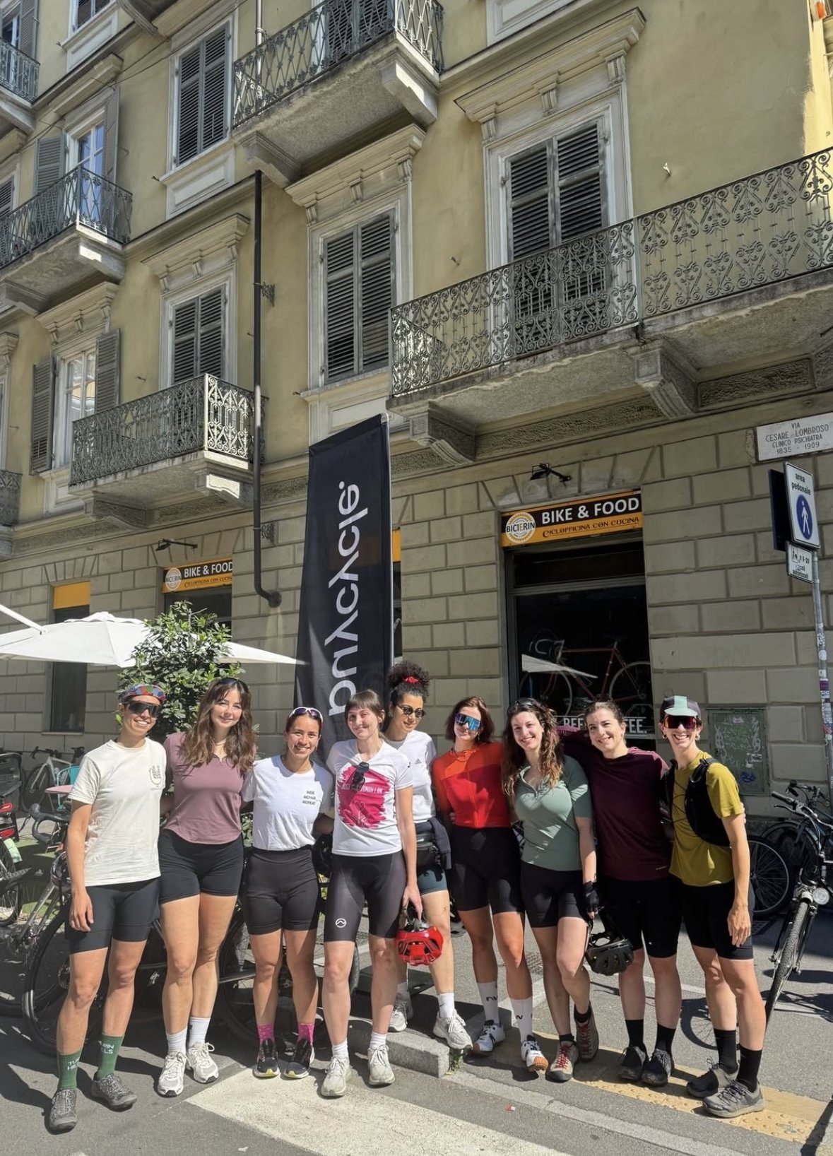 Ten women in cycling kit standing with their bikes outside a bike shop in Turin