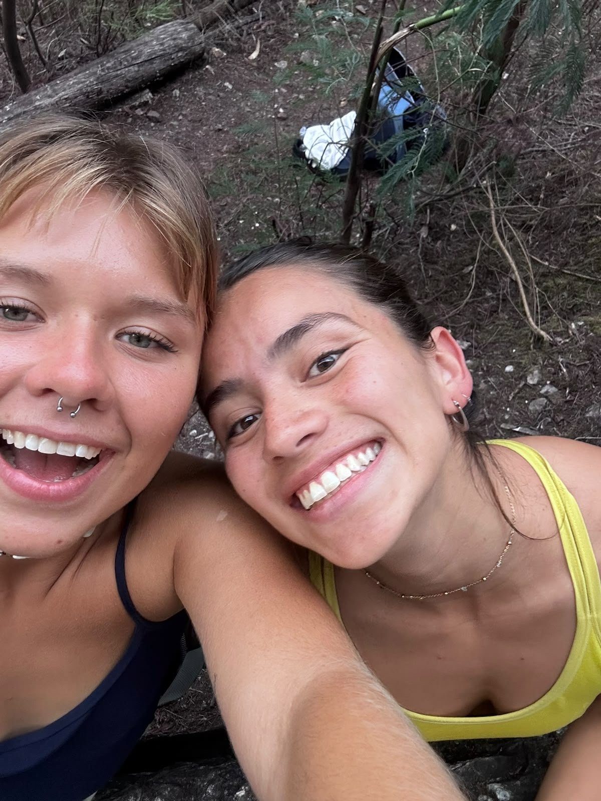 Two women leaning together outdoors after a climb, laughing at the camera