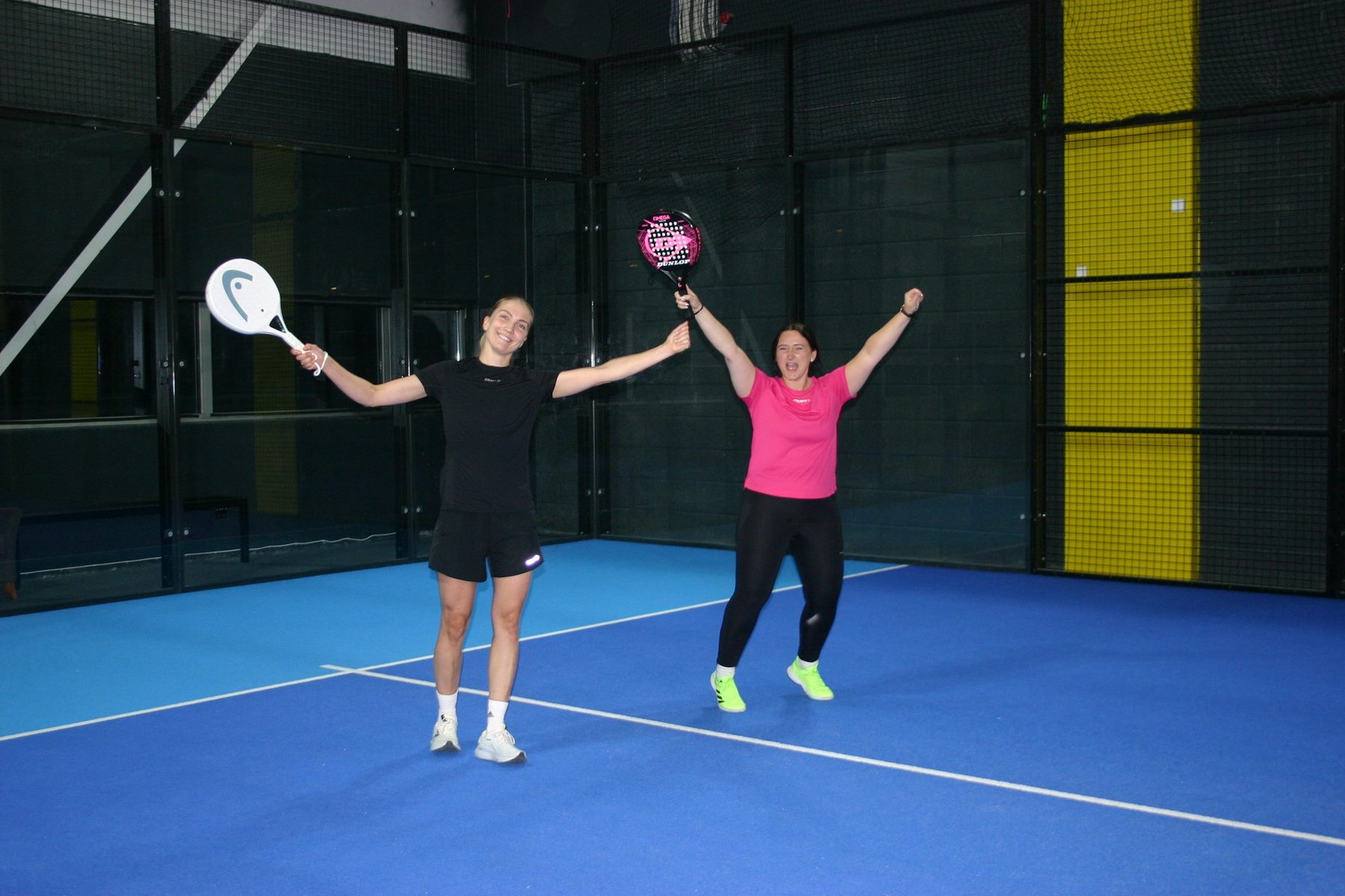 Two women celebrating with arms raised and padel rackets in hand on a blue court near Trondheim