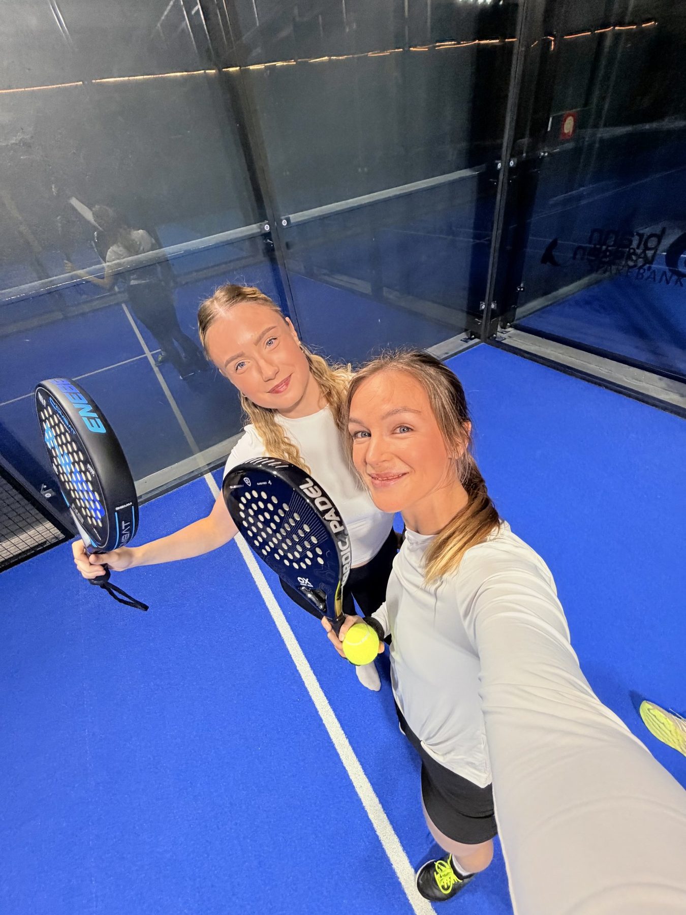 Two women taking a selfie together on a padel court, rackets in hand