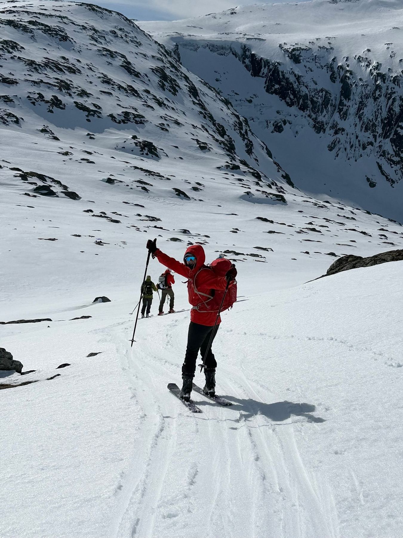 Three women ski touring across a snowfield beneath steep Norwegian peaks