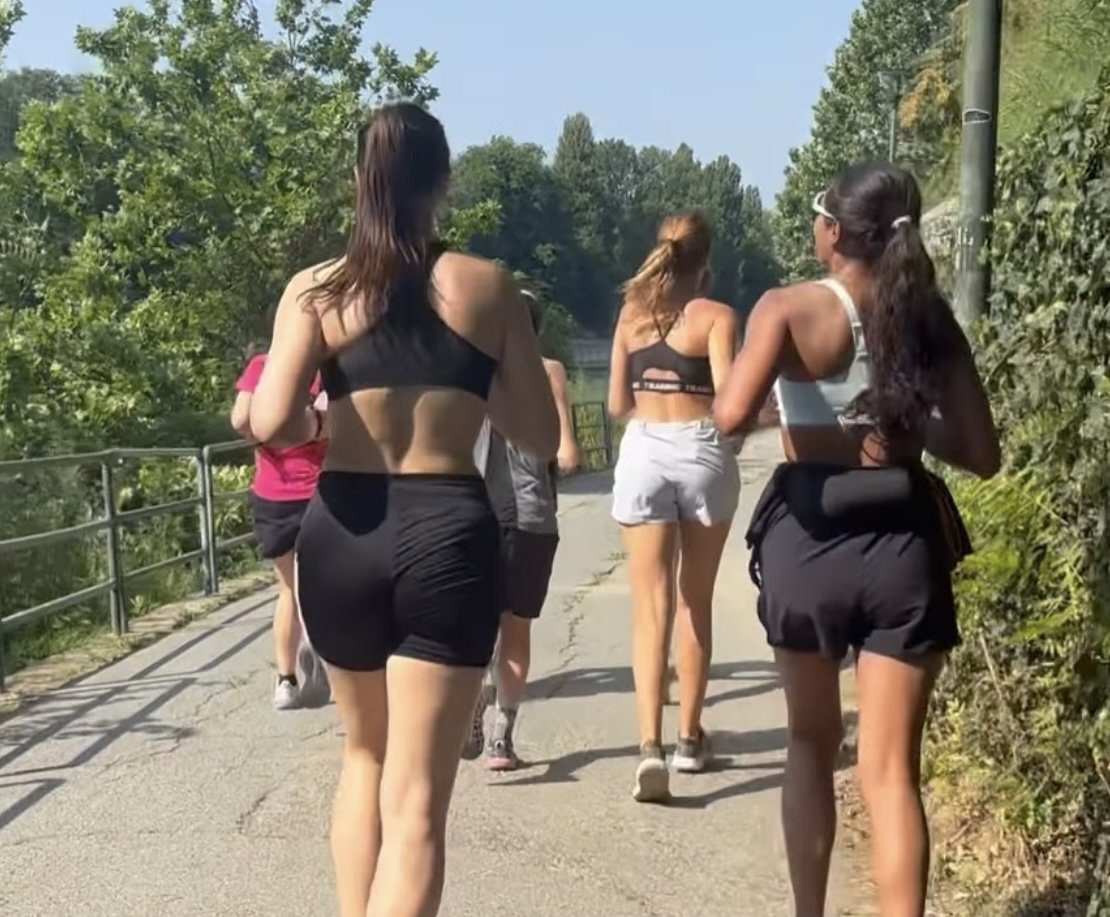 A group of women running away from the camera along a shaded path on a summer morning